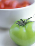 Whole Green Tomato in Front of a Bowl of Red Tomatoes Photographic Print by David Loftus