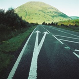 Two painted arrows on a road pointing towards a grassy mountain Photographic Print