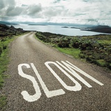 Road leading to the ocean with 'slow' painted on it Photographic Print