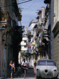 Woman with Baby, Man on Bicycle and Old Car in a Narrow Street Lined with Houses, Havana, Cuba Photographie par Rick Gerharter