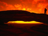 Silhouette of a Hiker on Mesa Arch Against a Spectacular Orange Sky, Utah, USA Photographic Print by Cheyenne Rouse
