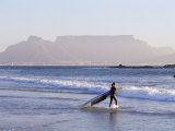 Young Woman Surfer Enters the Water of the Atlantic Ocean with Table Mountain in the Background Photographic Print by Yadid Levy