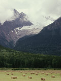 Glacier Descending from Clouded Mountains Contrasts with a Field Dotted with Rolls of Hay Photographie par Sylvia Sharnoff