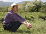 Man in Straw Hat Squats in a Field in the Chinese Countryside, Dajuhu, China Photographie par David Evans