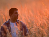 Young Man Stands in Tall Prairie Grass as the Sun Sets Photographie par Joel Sartore