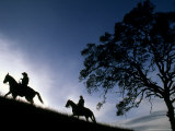 Silhouette of a Man and Woman Riding their Horses Up a Grassy Hill Photographie par Kate Thompson