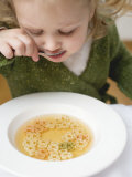 Small Girl Eating Soup with Teddy Bear Pasta Lámina fotográfica