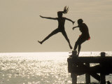 Silhouette of Girls Jumping off Pier Photographic Print by Anne Flinn Powell