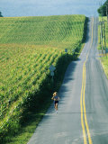 A Woman Jogs Down a Country Road Alongside a Field of Corn Lámina fotográfica por Skip Brown