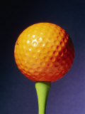 Une balle de golf orange sur un té vert et un fond bleu Photographie par Brian Gordon Green