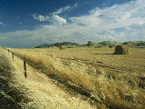 A Hay Field with Bales Sitting under a Cloud-Filled Sky Photographic Print