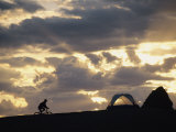 A Mountain Biker Cycles Toward Tents at a Campsite Photographie par Dugald Bremner
