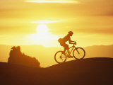 A Woman Rides Her Bike in the Sunset with Rock Cliffs in the Background Fotografisk trykk av Dugald Bremner