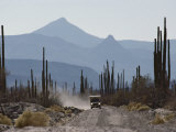 A Truck Travels Through a Landscape of Mountains and Saguaro Cacti Photographic Print by Annie Griffiths Belt