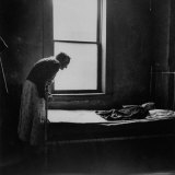 Daylight Cast from Window Reveals Old Woman Bent over the Foot of Bed Gazing Tenderly on Cloth Doll Photographic Print by Wallace Kirkland