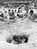 Couple Cuddling While Sitting in a Hole as Others Enjoy the Beach on the 4th of July Reproduction photographique sur papier de qualité par Ralph Crane