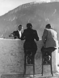 British Couple on High Stools at Ice Bar Outdoors at Grand Hotel as Waiter Pours Them Drinks Photographic Print by Alfred Eisenstaedt