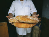 A Baker Shows His Fresh Loaves in the Village Bakery Photographic Print by Heather Perry