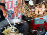Basket of Eggs Hanging in Front of Woman Cooking Asian Stir-Fry, Rapid Creek Market, Australia Photographic Print by Will Salter