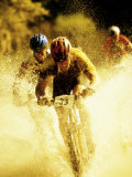 Young Men Riding Bicycles Through Water Fotografisk tryk Young Men Riding Bicycles Through Water Fotografisk tryk