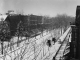Woman sweeps snow off a snow-covered street lined with brownstones near two horse-drawn buggies. Premium fotografisk trykk av George B. Brainerd Woman sweeps snow off a snow-covered street lined with brownstones near two horse-drawn buggies. Premium fotografisk trykk av George B. Brainerd