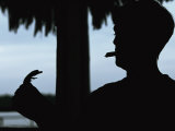 A Cigar-Smoking Cuban Man in Silhouette Holds a Baby Crocodile Photographic Print by Steve Winter