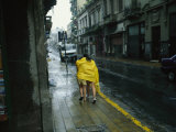 Two People Share a Raincoat as They Hurry Down a Rainy Street Photographie par Pablo Corral Vega