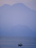 A Lone Boat Plies a Mountain Lake in Early Morning Fog Photographic Print by Raul Touzon