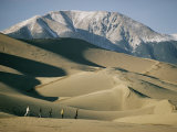 Hikers Among the Sand Dunes with a Snow-Covered Mountain Rising in the Background Photographie par Walter Meayers Edwards