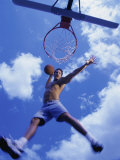 Low Angle View of a Young Man Slam Dunking a Basketball Lámina fotográfica