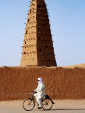Robed Tuareg Man Cycling Past Minaret of Mud-Brick Grande Mosquee, Agadez, Niger Photographic Print by Pershouse Craig