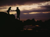 A Man with a Camera Helps a Woman Down Rocks Near Tanah Lot Temple Photographic Print by Justin Guariglia