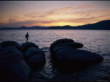 A Man Walks Along Large Rocks Jutting out into the Harbor Photographic Print by George F. Mobley