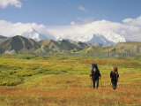 Man and Woman with Backpacks and Walking Sticks Cross Meadow Photographie