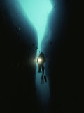 A Diver Swims Through a Large Crack in the Rock of Tgyiani Reef Photographic Print by Bill Curtsinger