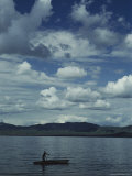 A Man Rows a Boat to Shore under a Cloud-Filled Sky Photographic Print by Bill Curtsinger