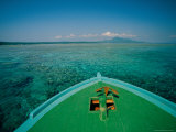 A boat anchored over a reef in clear water, with a mountain in distance. Lámina fotográfica A boat anchored over a reef in clear water, with a mountain in distance. Lámina fotográfica