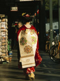 Kimono-Clad Geisha Walks Past Shops and Parked Bicycles; she is a Maiko or Apprentice Geisha Photographic Print