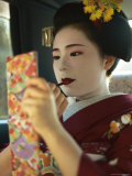 A Kimono-Clad Geisha Applies Lipstick in the Back of a Cab Lámina fotográfica por Justin Guariglia