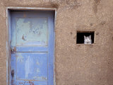 Next to a Blue Door, a Cat Peers Out of the Window of an Adobe House Photographic Print