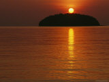 The Sun Casts a Red Glow and a Reflection as It Sets Behind an Island Photographic Print by Nicolas Reynard