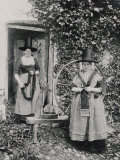 Two Welshwomen in Traditional Dress Stand Outside Their Cottage with a Spinning Wheel Lámina fotográfica