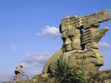 Cyclist Riding Past a Stone Sculpture Photographic Print