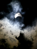 The Moon Partially Covers the Sun Behind the Clouds During a Partial Solar Eclipse Photographic Print