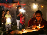 A Woman Lights Earthen Lamps as Children Ignite Firecrackers in New Delhi Photographic Print by Manish Swarup