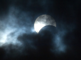 Seen Through Clouds the Sun is Partially Obscured by the Moon During an Eclipse Photographic Print