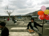 An Afghan Boy Sits on a Grave Plot and Sells Balloons and Eggs as Others Relax Photographic Print