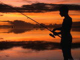 The Silhouette of a Boy Fishing at Sunset in One of the Lagoons Around the Island, Cook Islands Photographic Print by Dallas Stribley