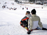 Two People on Sled at Top of Run with People Below Photographic Print by Brian Cruickshank