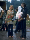 Couple Standing Barefoot on a Road Holding a Bundle and Wine Bottle, Woodstock Music and Art Fair Lámina fotográfica por John Dominis Couple Standing Barefoot on a Road Holding a Bundle and Wine Bottle, Woodstock Music and Art Fair Lámina fotográfica por John Dominis